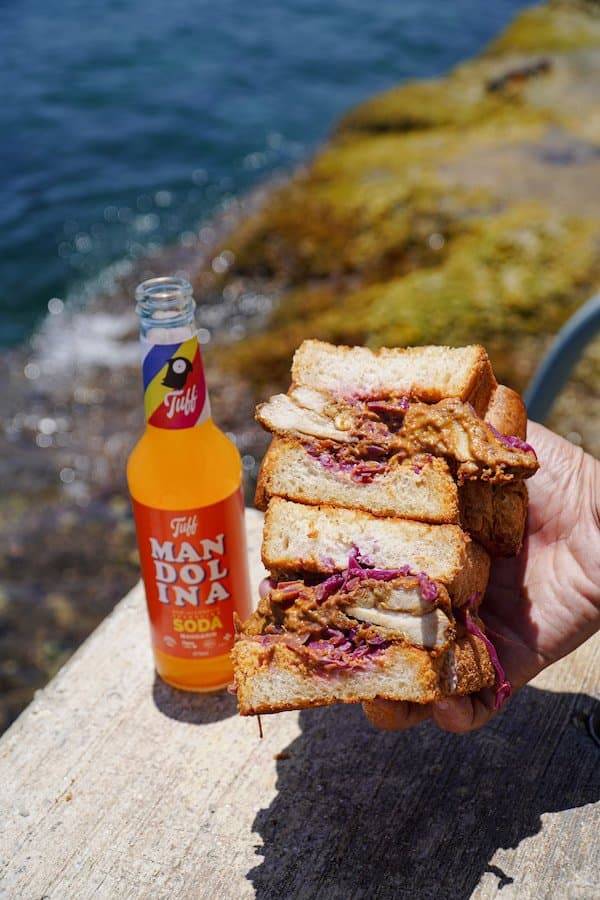 Fuwamai XL chicken sando with red cabbage slaw on Japanese milk bread beside a Tuff Mandolina soda by the sea in Malta
