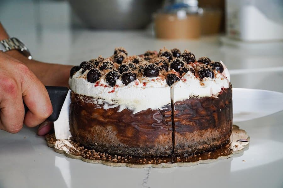 Fuwamai Black Forest Basque cheesecake topped with cherries and whipped cream being sliced